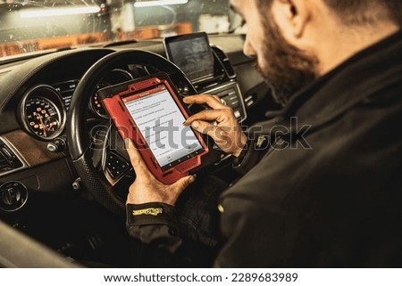 A mechanic's hands use a diagnostic tool to troubleshoot a modern car's computer system in a garage. Royalty-Free Stock Photo #2289683989