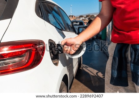 Man opening the car nozzle to refuel gasoline or diesel fuel in a white car. Concept of transportation, energy crisis, oil crisis. Full tank in the midst of a price crisis at the gas pump