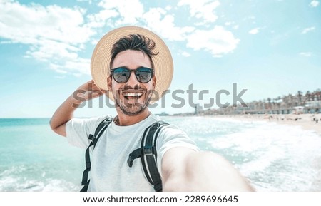 Happy man with hat and sunglasses taking selfie picture with smartphone at the beach - Cheerful traveler having fun outside - Handsome guy smiling at camera