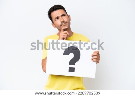 Young handsome man over isolated white background holding a placard with question mark symbol and thinking Royalty-Free Stock Photo #2289702509