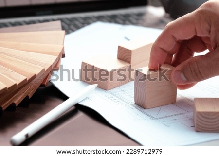 A designer is laying a piece of sketching paper on a computer table with a block of wood on it. The idea is to choose materials for house décor, and there is wood that is used as a color sample.