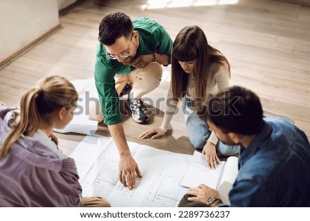 Young architects sitting on the floor and  analyzing blueprints  in the office
