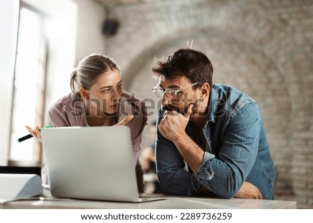 Young  man talking to his female colleague while working on laptop in the office