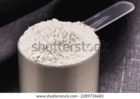 casein in measuring spoon, black background with weights and weight training dumbbells, macrophotography