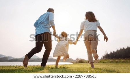 Happy family in the park sunset light. family on weekend running together in the meadow with river Parents hold the child hands.health life insurance plan concept. Royalty-Free Stock Photo #2289738565
