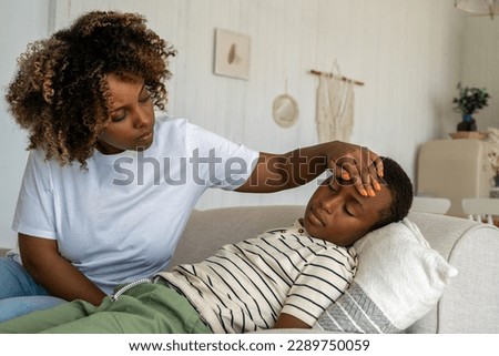 Loving African American mother taking care of sick child at home, worried parent mom checking temperature touching forehead of unhealthy sleeping on sofa schoolboy son. Treating colds in children Royalty-Free Stock Photo #2289750059
