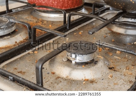 Dirty gas stove top with food leftovers. Unclean steel kitchen cooktop with greasy spots. Spring-cleaning, remove kitchen old fat stains, fry spots, oil splatters and burned-on bits. Selective focus. Royalty-Free Stock Photo #2289761355