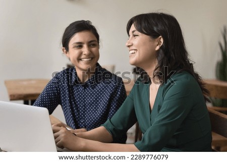 Indian and Armenian women talking, working together on project having friendly conversation, share ideas engaged in creative team-work use laptop seated at desk, communication, teamwork, friendship Royalty-Free Stock Photo #2289776079