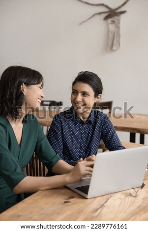 Multi ethnic women colleagues laughing in office at workplace desk, share thoughts, ideas, opinions enjoy break and pleasant informal talk during workday, having successful teamwork, enjoy friendship Royalty-Free Stock Photo #2289776161