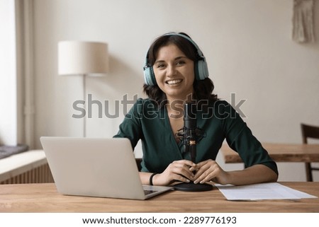 Woman radio host in headphones sit at desk with microphone and laptop, take part in online conference, videocall, look at camera. Portrait of blogger, influencer, streamer, record webinar or podcast