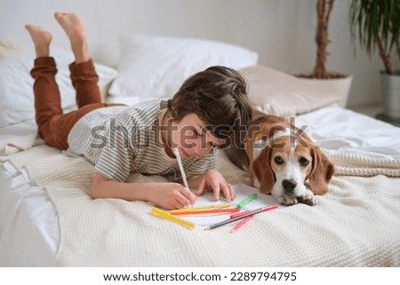 young boy engrossed in drawing with colorful pencils, while his loyal beagle companion lies beside him, illustrating the nurturing environment necessary for fostering creativity in children. Royalty-Free Stock Photo #2289794795