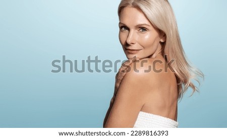 Mature old lady with beautiful glowing body and face, looks behind her shoulder with confident gaze, has perfect skin, applies anti-aging skincare cream and cosmetic products for nourished face Royalty-Free Stock Photo #2289816393