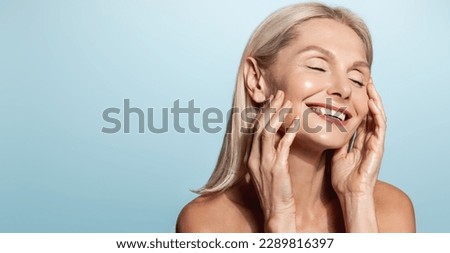 Gorgeous senior older woman with closed eyes touching her perfect skin. Beautiful portrait mid 50s aged woman advertising facial antiage lift products salon care tighten skin isolated on blue. Royalty-Free Stock Photo #2289816397