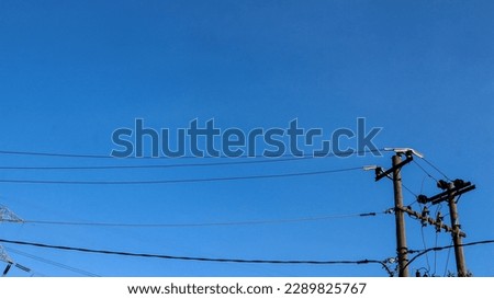 Electric wires and electric poles crossing the high voltage pole tower against the blue sky background.