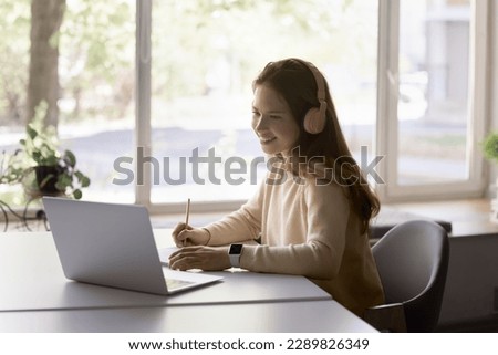 Pretty teen girl wear headphones use laptop e-learns subject, improve foreign language skills, gain new knowledge online. Tuition, videocall event with tutor, helps with exercise. Tuition, modern tech Royalty-Free Stock Photo #2289826349
