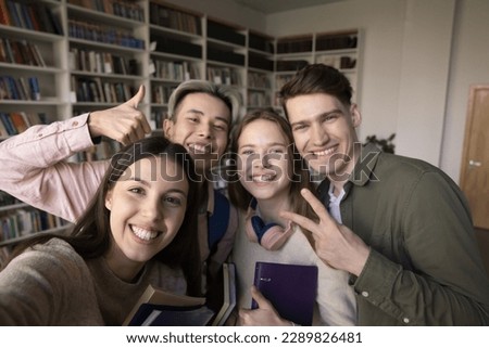 Multiethnic best friends, girls and guys, students standing in library looking at smartphone screen make selfie picture, gesturing, record vlog for channel. Generation Z, modern tech, studentship, fun Royalty-Free Stock Photo #2289826481