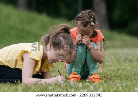 Two 8 years old girls playing together in park. One girl wearing glasses drawing. One girl crying.