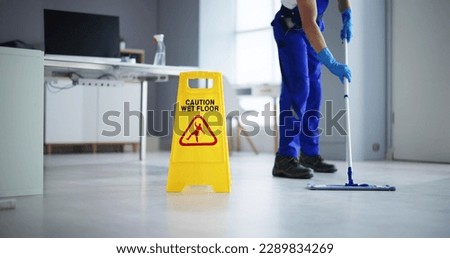 Low Section Of Male Janitor Cleaning Floor With Caution Wet Floor Sign In Office