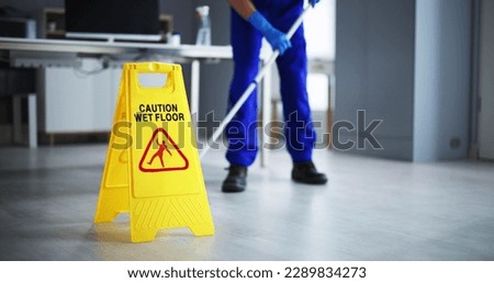 Low Section Of Male Janitor Cleaning Floor With Caution Wet Floor Sign In Office Royalty-Free Stock Photo #2289834273