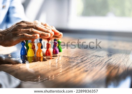 Inclusion, Diversity And Equality. African Hands Safeguard Wooden pawns Royalty-Free Stock Photo #2289836357