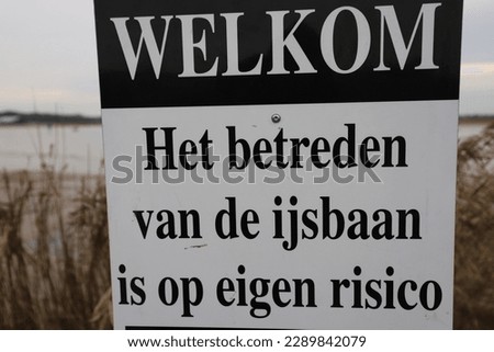 A sign in a winter landscape with a Dutch text that says, welcome, entering the ice rink at your own risk.