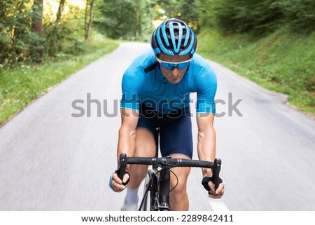Man pedaling on a racing bike downhill in body position with straight arms and hands in the drops position on handlebars