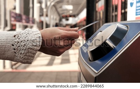Female hand holding a card on contactless card reader machine in train station in London. There a blurry red train in the station. No cash public transport concept. Royalty-Free Stock Photo #2289844065
