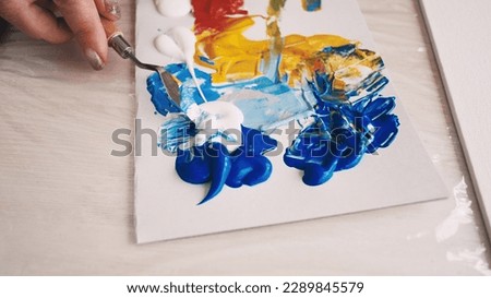 Art studio. Female artist. Creative process. Unrecognizable woman mixing paints colors for creating picture on canvas with spatula.