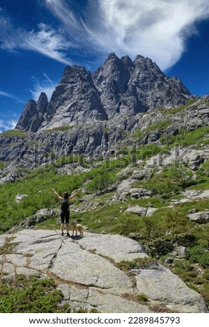 Woman hikes with dog in Restonica valley. View of the peaks of the Restonica mountains and a hiking trail where a young woman is walking with a dog, Lac du Melu, Corsica island, France