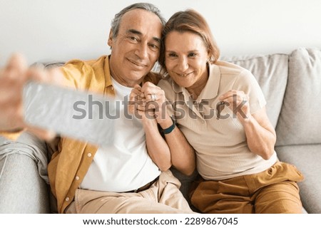 Happy european spouses taking photo on smartphone and showing keys, video calling and talking about buying apartment, sitting on sofa. Love, relationship, selfie for blog and social networks