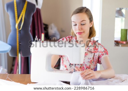 Young attractive needlewoman at studio working with sewing machine