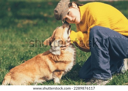 Portrait of a caucasian woman in yellow sweater and checkered cap with corgi dog. Corgi dog kissing his owner High quality photo