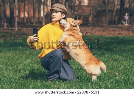 Friendship Concept. Excited beautiful caucasian woman taking selfie with her welsh corgi pemroke dog in the park,corgi licking her face. High quality photo