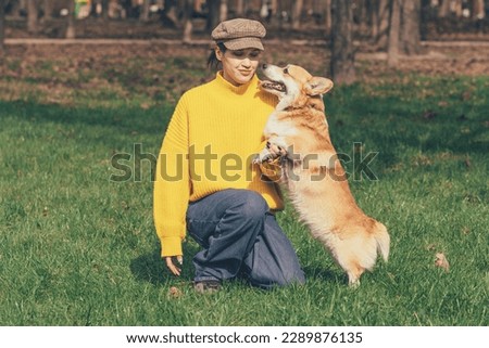 Portrait of a caucasian woman in yellow sweater and checkered cap with corgi dog. High quality photo