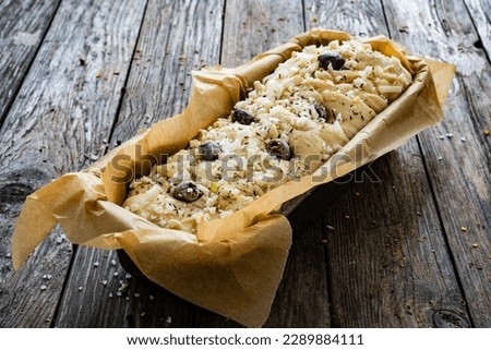Loaf of village, uncooked bread with feta and black olives on wooden table 