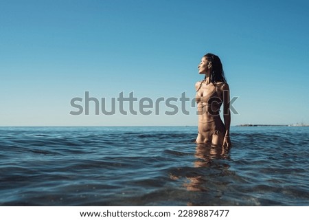 young beautiful girl in a swimsuit stands in the sea and enjoys 