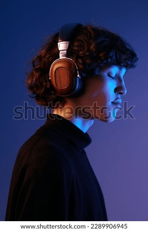 Man wearing headphones listening to music with his eyes closed, enjoying the sound, hipster lifestyle blogger, portrait purple background, mixed neon light, fashion style and trends, copy space Royalty-Free Stock Photo #2289906945