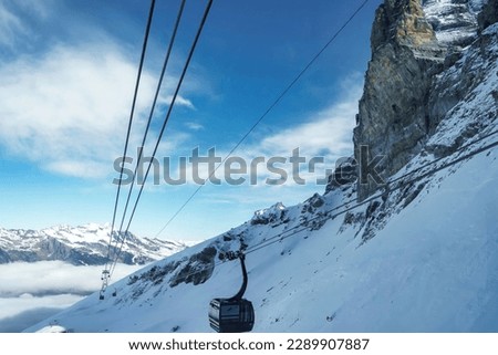 Gondola lift moving on cable over beautiful snowcapped Bernese mountain under cloudy sky at ski resort in Jungfrau, Switzerland, winter holiday and nature concept