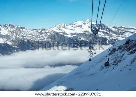 Gondola lifts moving on cables over snow covered hill with beautiful snowcapped Bernese mountains under sky at ski resort in Jungfrau, Switzerland, winter holiday and nature concept