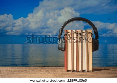 Set of books, headphones and eyeglasses on wooden table near sea water on the beach, close up. Audiobooks and education concept
