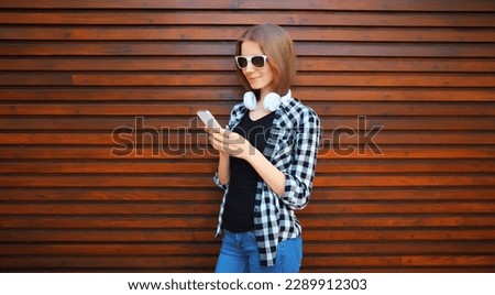 Portrait of teenager girl listening to music in headphones looking at phone on brown wooden wall background