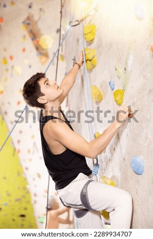 young muscular guy, insured by trainer, ascend up artificial climbing wall indoors. rappelling athlete Royalty-Free Stock Photo #2289934707
