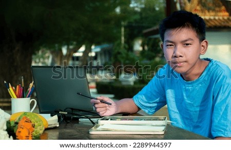 Asian boy in blue t-shirt sitting and spending his free time with drawing pictures by using watercolor, concept for summer vacation of teenagers around the world.