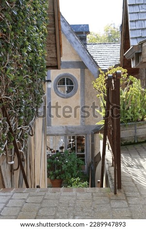 One of the several hidden passage ways in Carmel-by-the-Sea, with stairs leading down to a quaint building with a peaked roof and circular window. Royalty-Free Stock Photo #2289947893