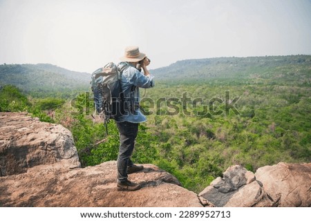 Photographer with backpacks relaxing on top of a mountain and enjoying the view of valley. Young man with camera and backpack enjoying sunset on the peak of mountain .Travel hiking. freedom concept.