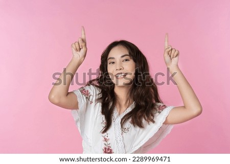 Young Asian woman pointing fingers to empty space isolated pink color background