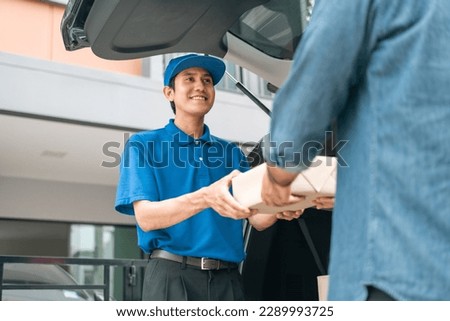 Asian delivery man with parcel in hand of blue uniform sending parcel to customer front of the house from shopping online with good service. Courier man send a package to destination.