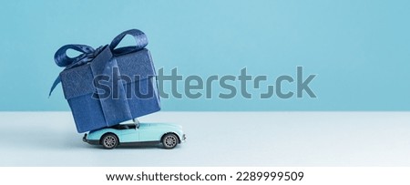 small Luxury gift box with a blue bow on on top of retro toy car. Side view monochrome. Fathers day or Valentines day gift for him. Corporate gift concept or birthday party. Festive sale delivery Royalty-Free Stock Photo #2289999509