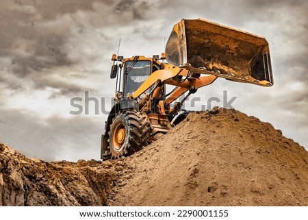 Powerful wheel loader or bulldozer working on a quarry or construction site. Loader with a full bucket of sand against the sky. Powerful modern equipment for earthworks Royalty-Free Stock Photo #2290001155