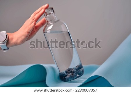 A woman's hand reaches for a glass bottle of water with blueberries. Royalty-Free Stock Photo #2290009057